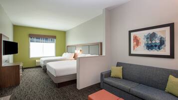 Quarto de hotel com cama, sofá, televisão e um quadro na parede.