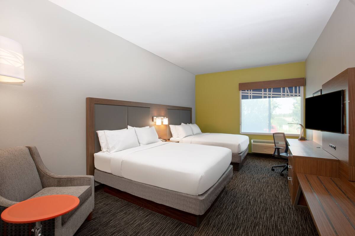 Ein Hotelzimmer mit zwei Betten, einem Schreibtisch, einem Stuhl, einem Fernseher und einem Fenster.