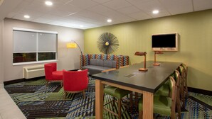 A conference room with a long table, red chairs, a sofa, and a television. - Holiday Inn Express Hotel & Suites Columbus by IHG (Columbus)
