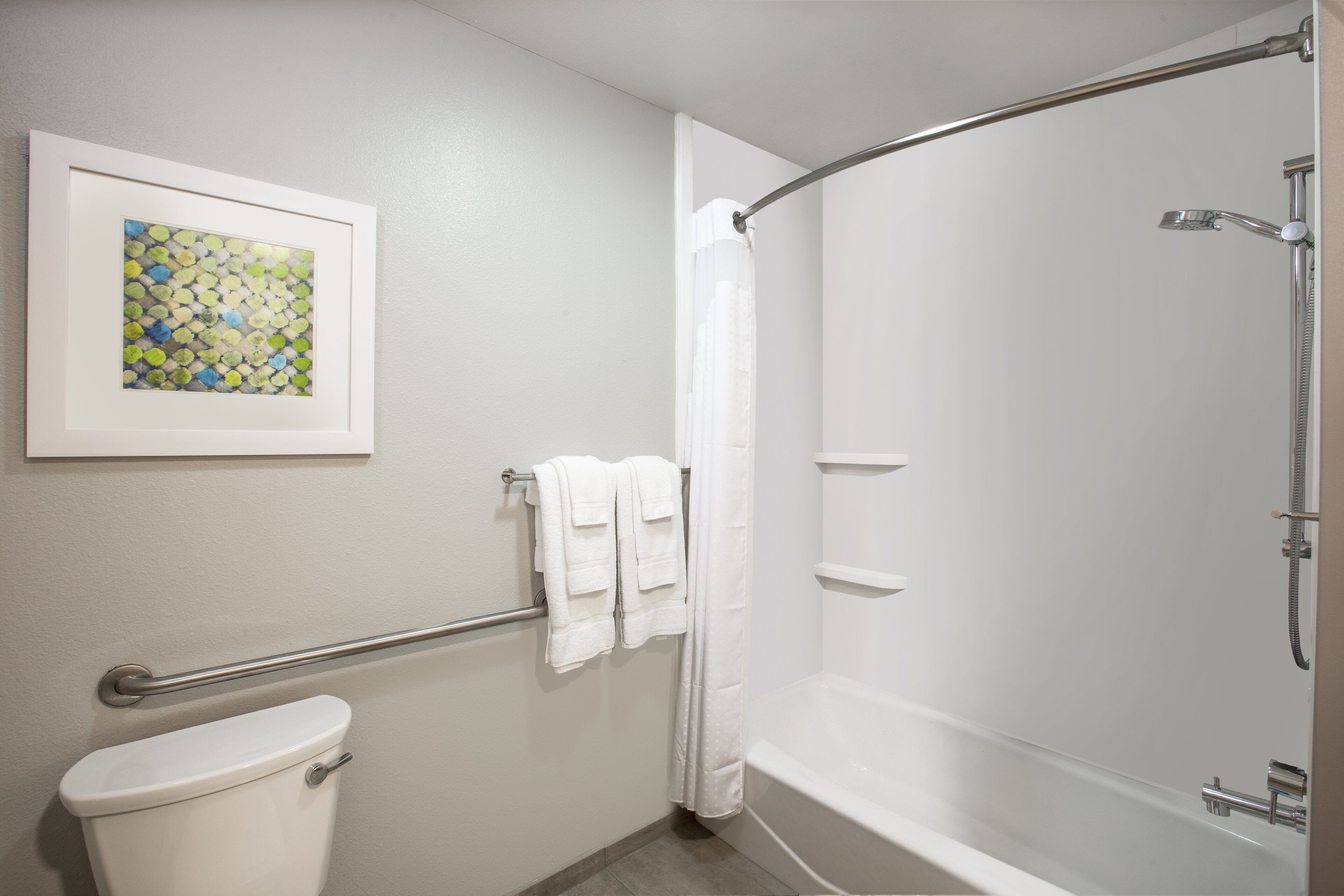 Et badeværelse med toilet, en bruseniche med buet glasdør, et håndklædetørrestativ med hvide håndklæder og et billede i ramme på væggen.