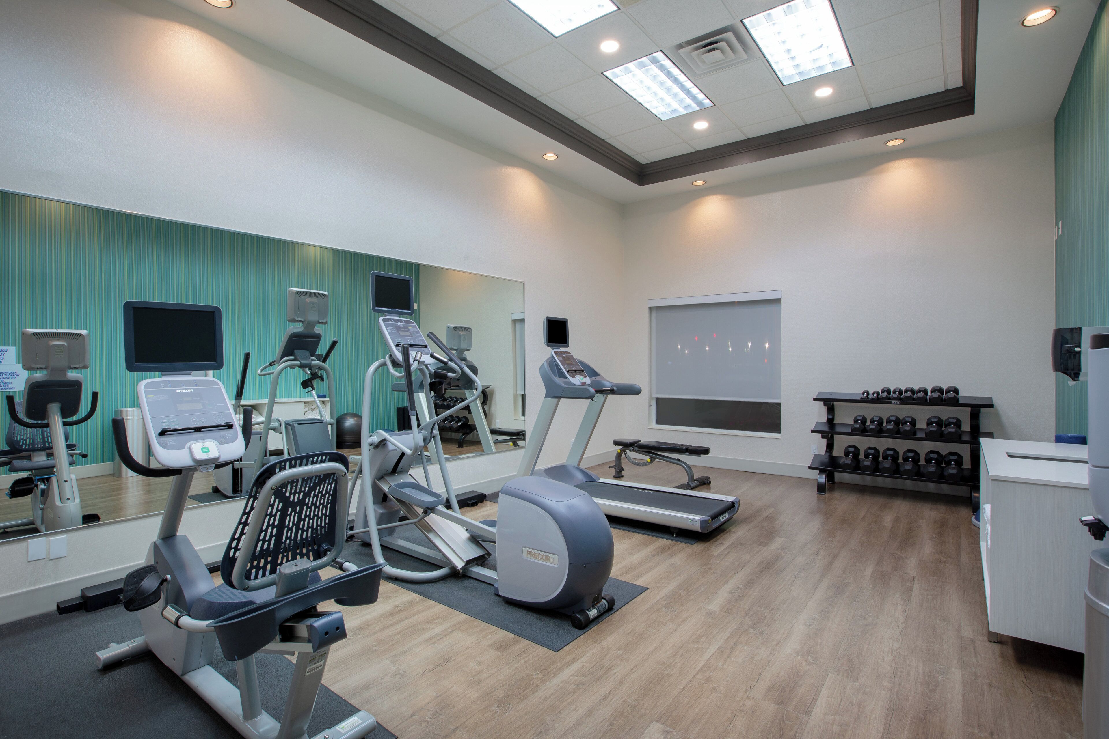 A gym with cardio machines, weight benches, and a mirror wall.