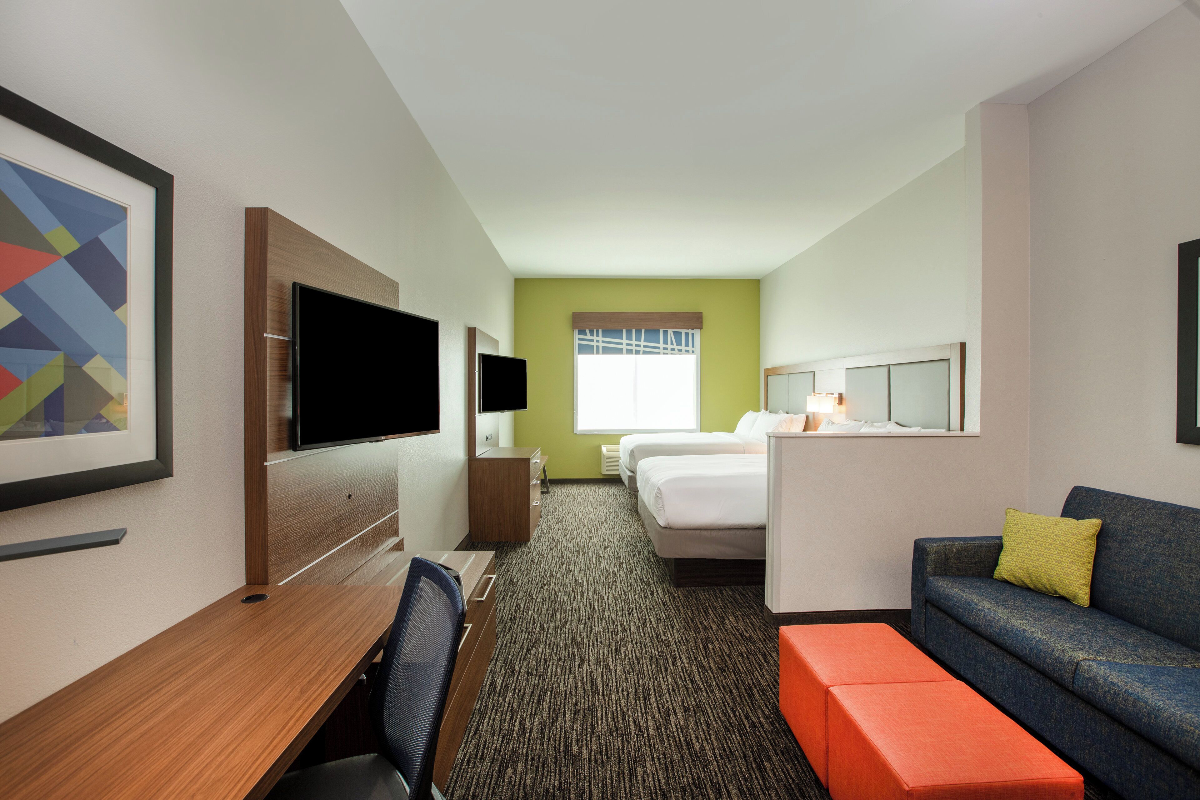A hotel room with a bed, a desk with a chair, a television, and a sofa.