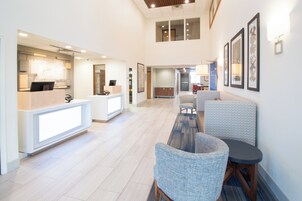 Un hall de hotel con mostrador de recepción, zona de estar y una escalera que conduce a un nivel superior.