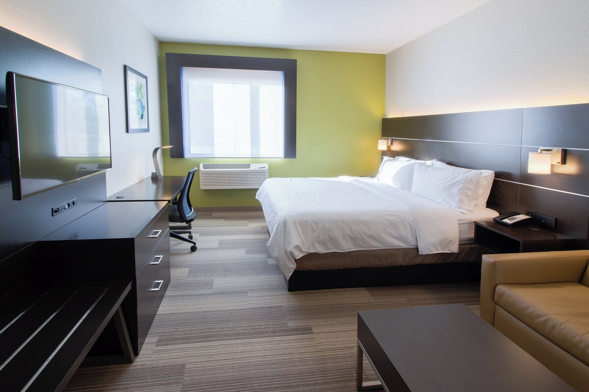 Ett hotellrum med en säng, ett skrivbord, en stol, en tv och ett fönster.