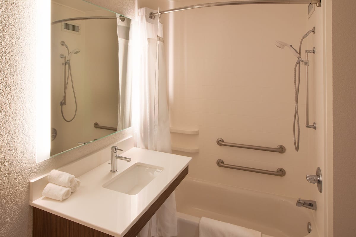 Un baño moderno con cabina de ducha de vidrio, un lavabo con espejo y barras de apoyo para mayor seguridad.