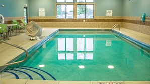 Une piscine intérieure à l’eau claire, entourée d’un sol carrelé et d’une rambarde de sécurité. Des fenêtres permettent à la lumière naturelle d’entrer, et un panneau indique la capacité maximale de la piscine.