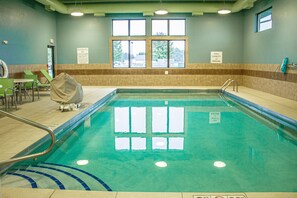 Une piscine intérieure à l’eau claire, entourée d’un sol carrelé et d’une rambarde de sécurité. Des fenêtres permettent à la lumière naturelle d’entrer, et un panneau indique la capacité maximale de la piscine.