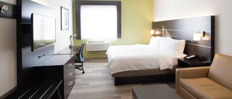 A hotel room with a bed, a desk with a chair, a television, a sofa, and a bedside table with a lamp.