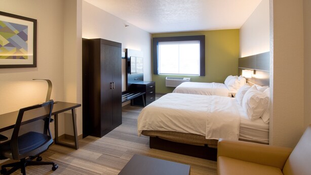 Une chambre d’hôtel avec deux lits, un bureau, une chaise, un canapé et une fenêtre avec des stores.