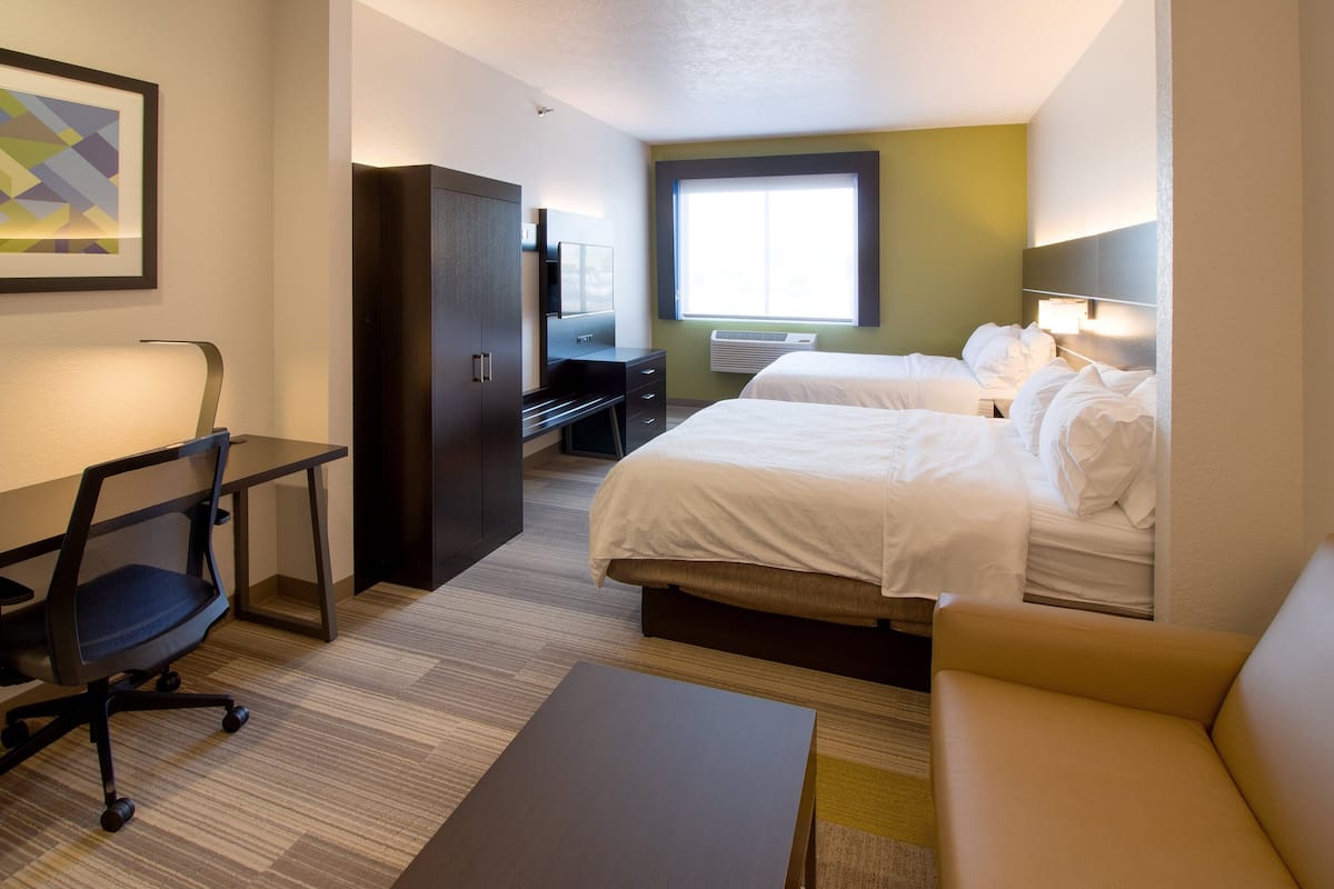 Habitación de hotel con dos camas, un escritorio, una silla, un sofá y una ventana con persianas.