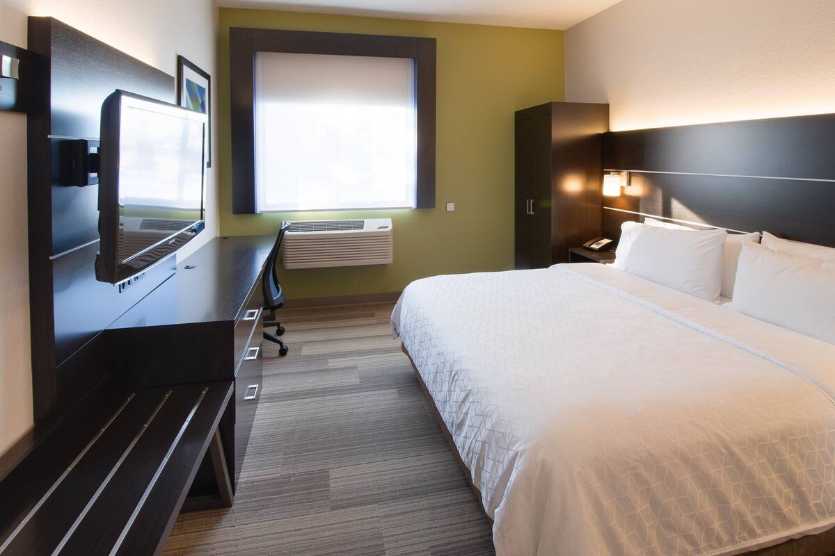 Habitación de hotel con una cama, un escritorio con computadora, un televisor, una ventana y un equipo de aire acondicionado.