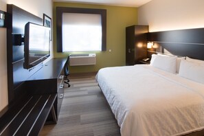 Habitación de hotel con una cama, un escritorio con computadora, un televisor, una ventana y un equipo de aire acondicionado.