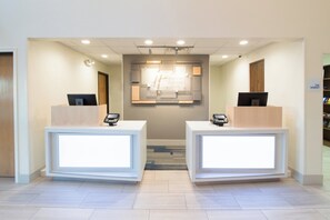 A hotel reception area with two reception desks, a central wall-mounted sign, and a carpeted floor.