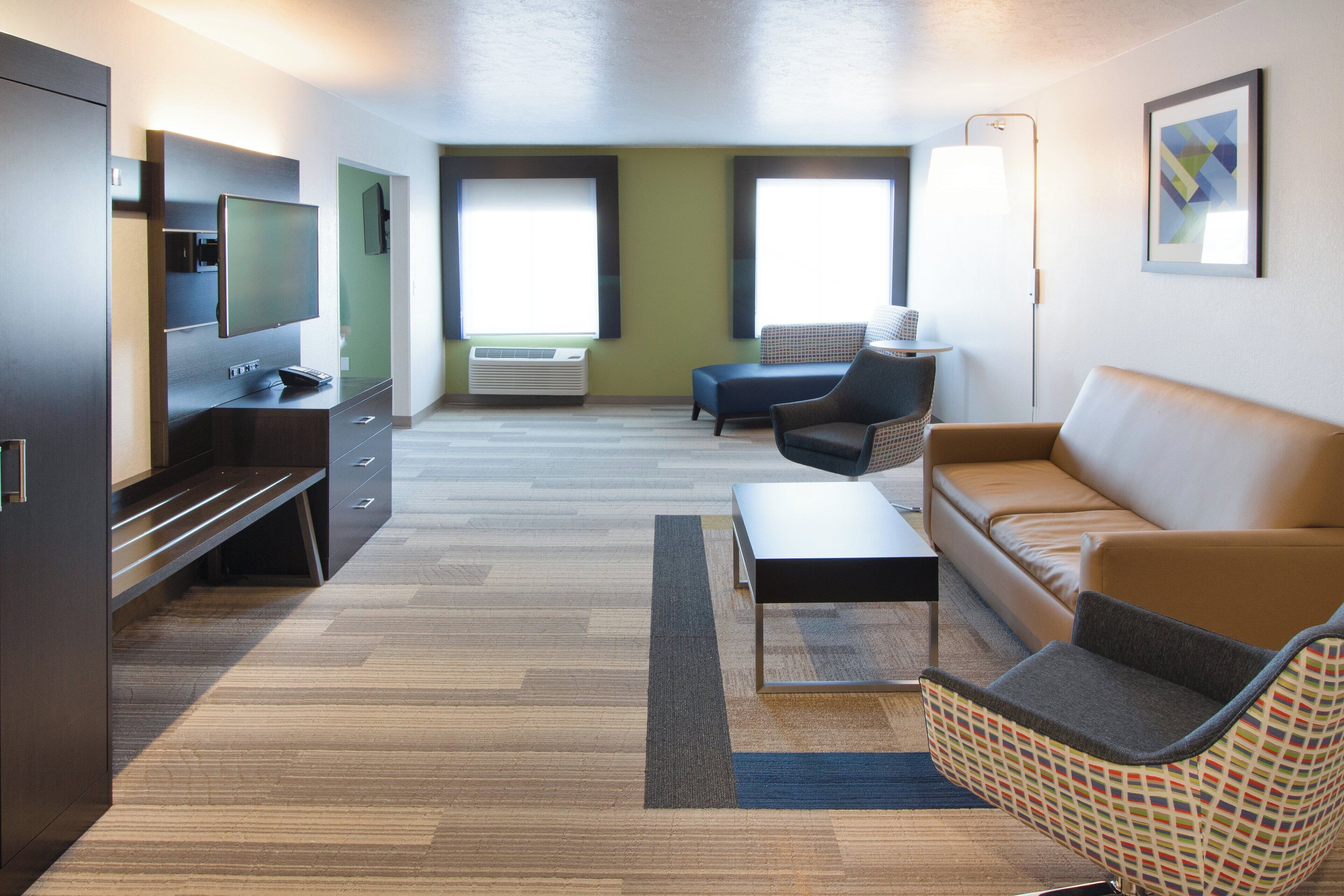 A modern hotel room with a flat-screen TV, a sofa, a chair, a small table, and a large window.