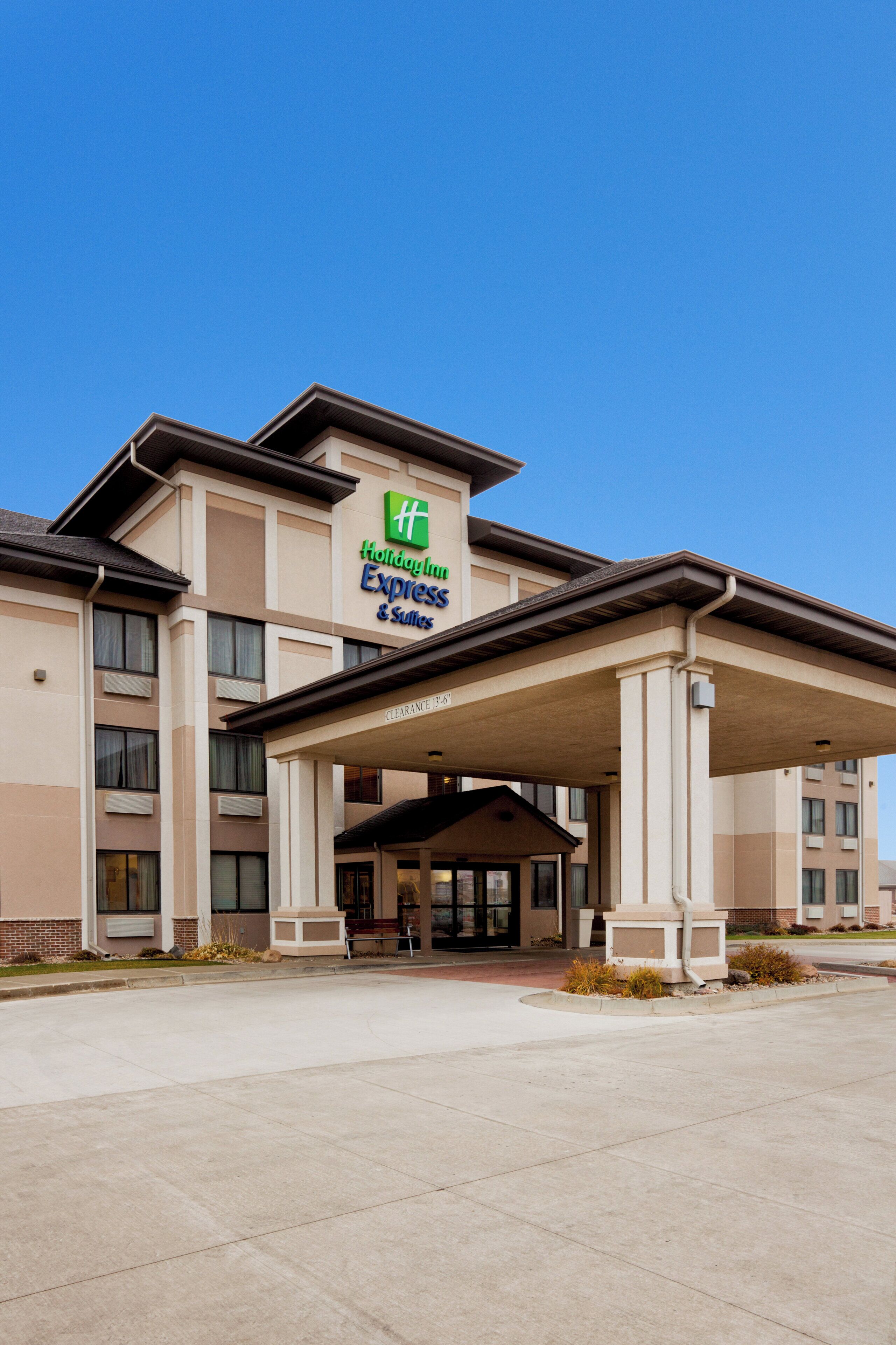 Un bâtiment de la chaîne Holiday Inn Express & Suites, doté d’une entrée abritée et surplombant un ciel d’un bleu limpide.