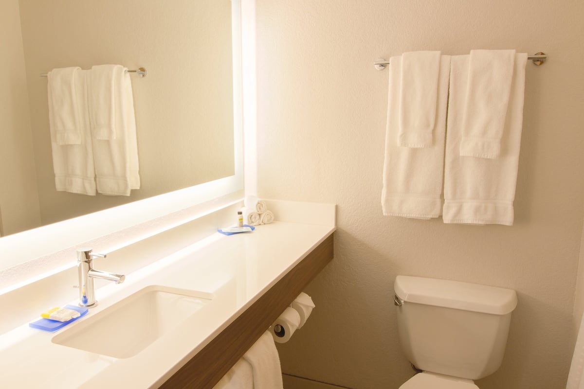 Un baño con lavamanos, espejo, toallero y retrete.