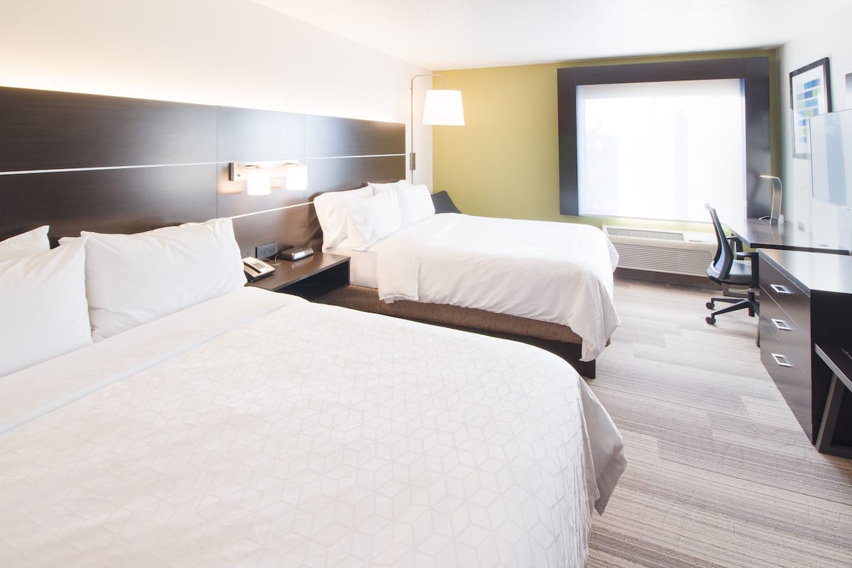 Habitación de hotel con dos camas, un escritorio, una silla, una lámpara y un ventanal grande.