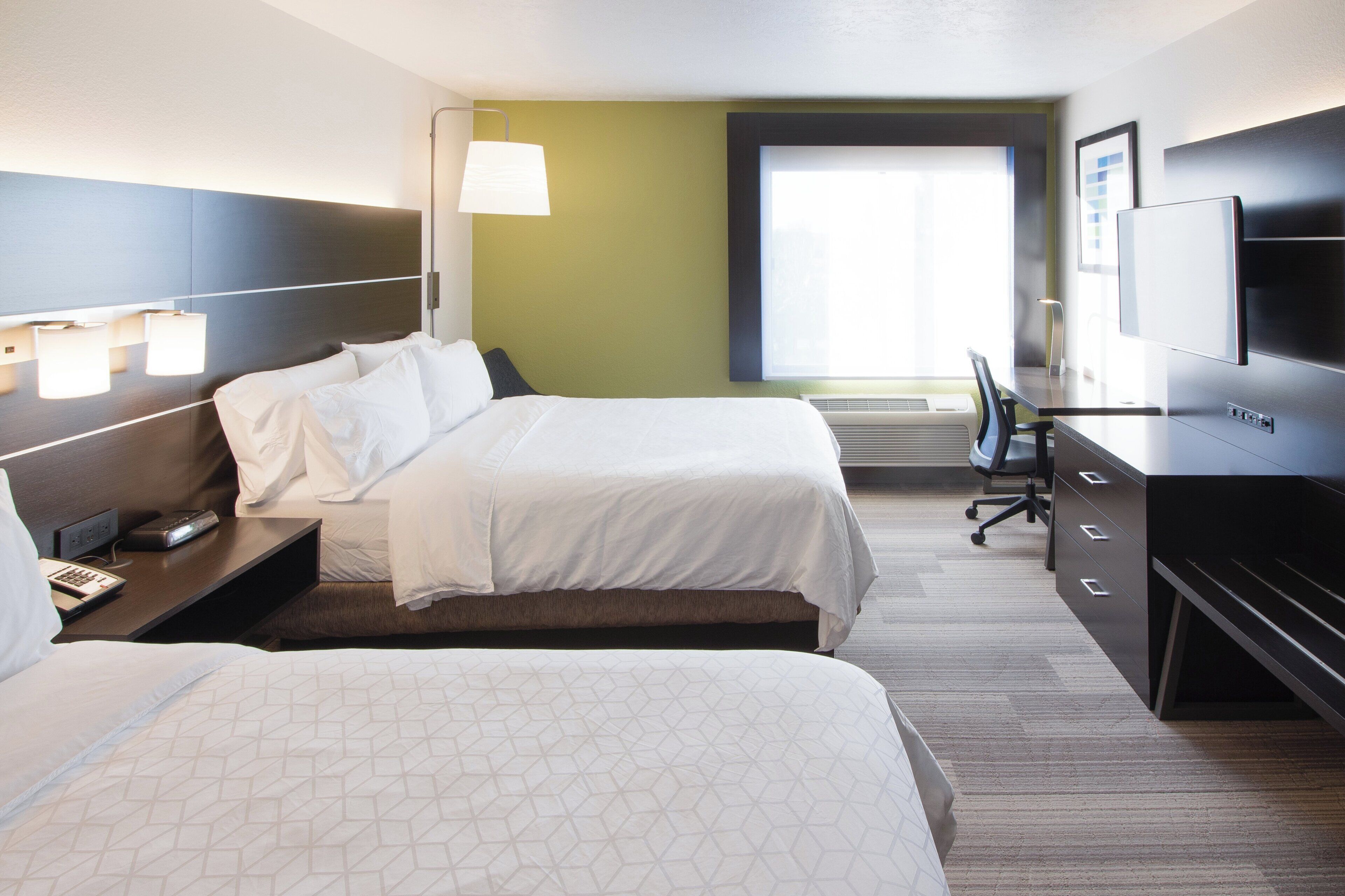 A hotel room with two beds, a desk, a chair, a television, and a window with blinds.