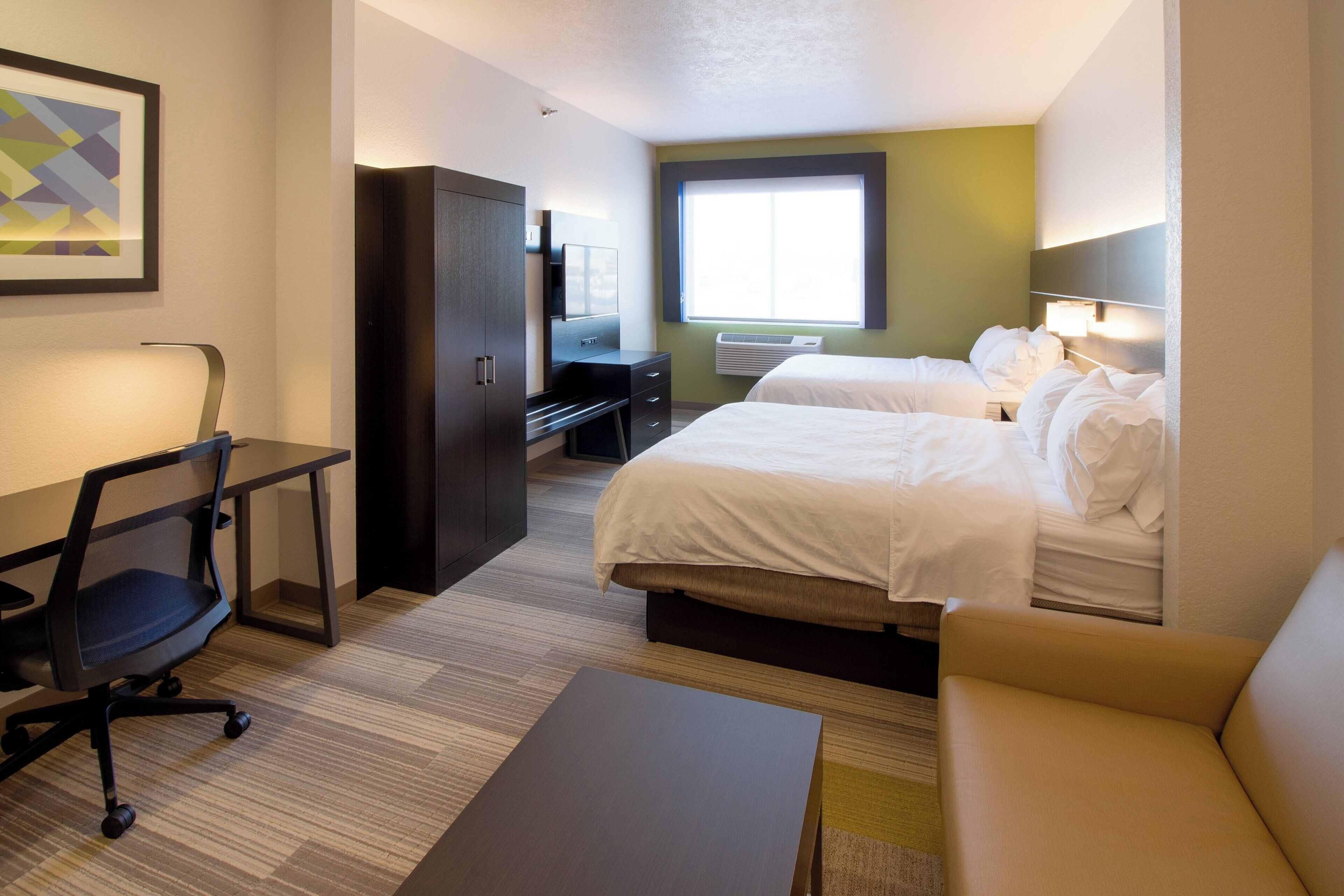 A hotel room with two beds, a desk, a chair, a couch, and a large window.