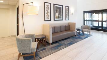 A lobby with a sofa, two armchairs, a floor lamp, and framed artwork on the wall.