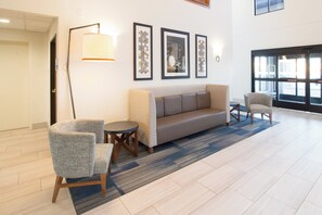 A lobby with a sofa, two armchairs, a floor lamp, and framed artwork on the wall. - Holiday Inn Express & Suites Worthington by IHG (Worthington)