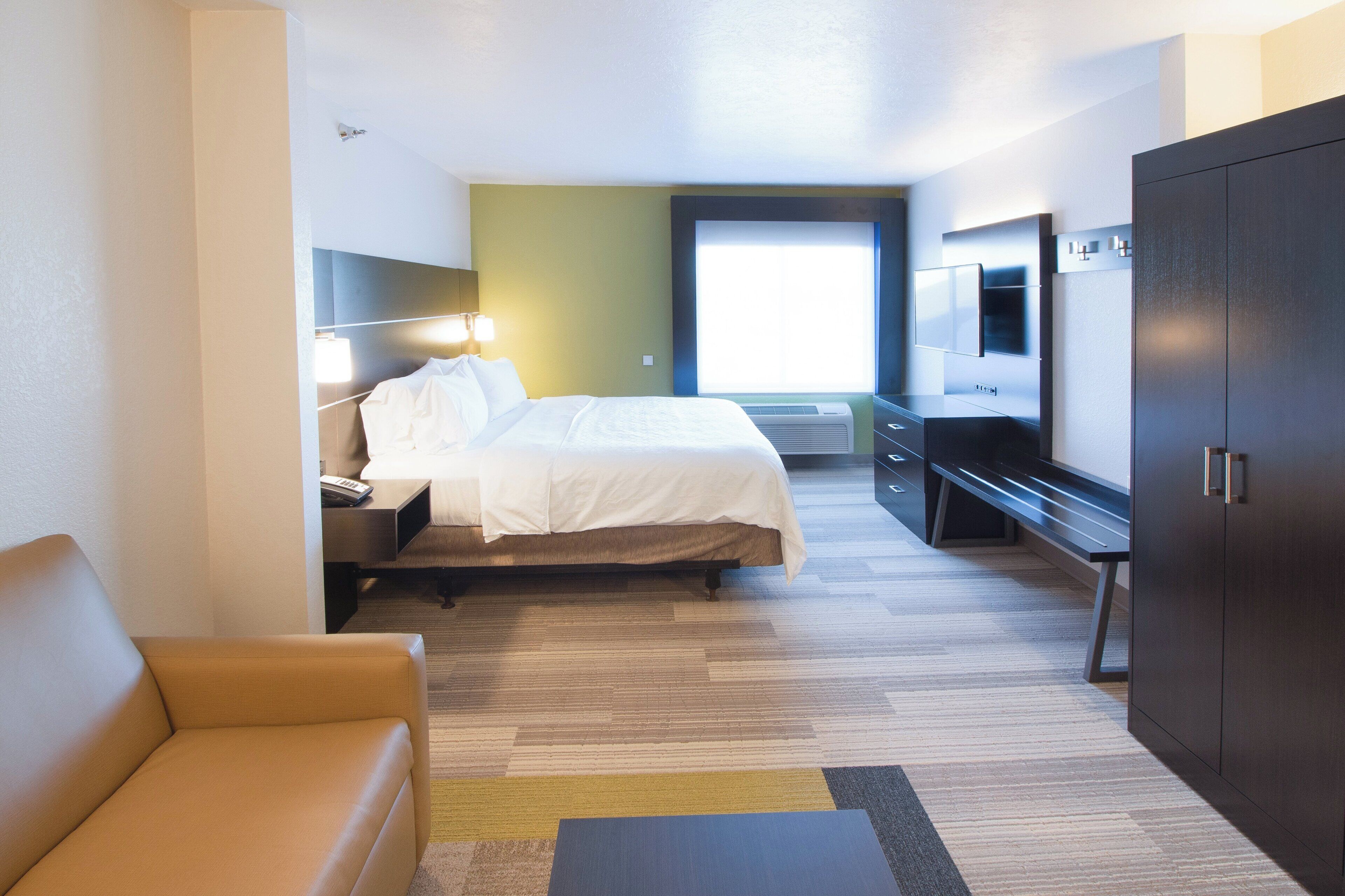 A hotel room with a bed, bedside table, lamp, TV, wardrobe, and a sofa.