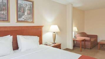 A hotel room with a bed, two bedside tables, a lamp, a chair, and two framed pictures on the wall.