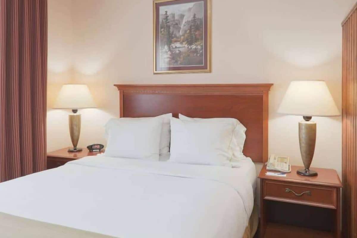 A hotel room with a large bed, two bedside tables with lamps, a wooden headboard, and a framed picture on the wall.