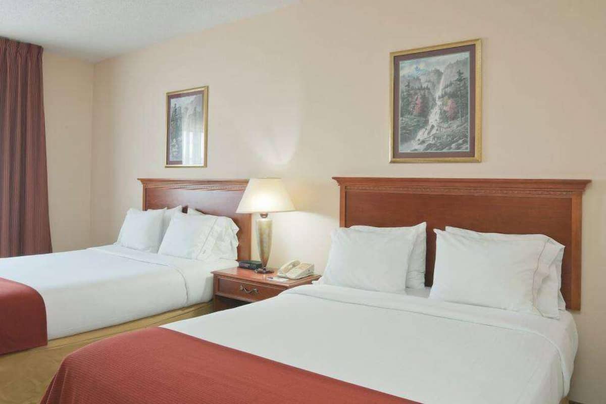 A hotel room with two beds, a nightstand with a lamp, and two framed pictures on the wall.