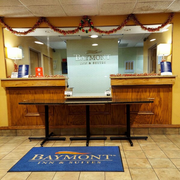 A reception area with a Baymont Inn & Suites sign, two reception desks, a blue doormat, and a Christmas garland.