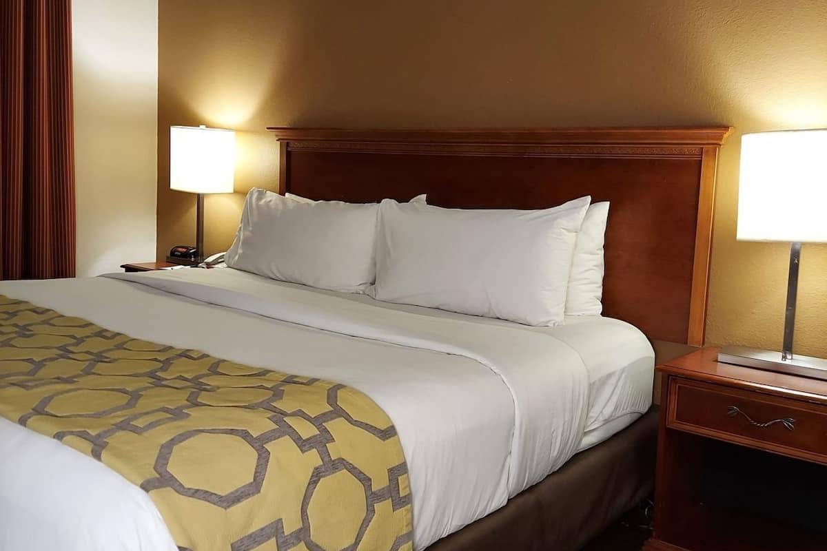 A hotel room with a large bed, two bedside tables, a wooden headboard, and a patterned throw blanket.