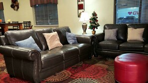 Un salon avec deux canapés en cuir, un pouf rouge, un sapin de Noël et un tapis à motifs.