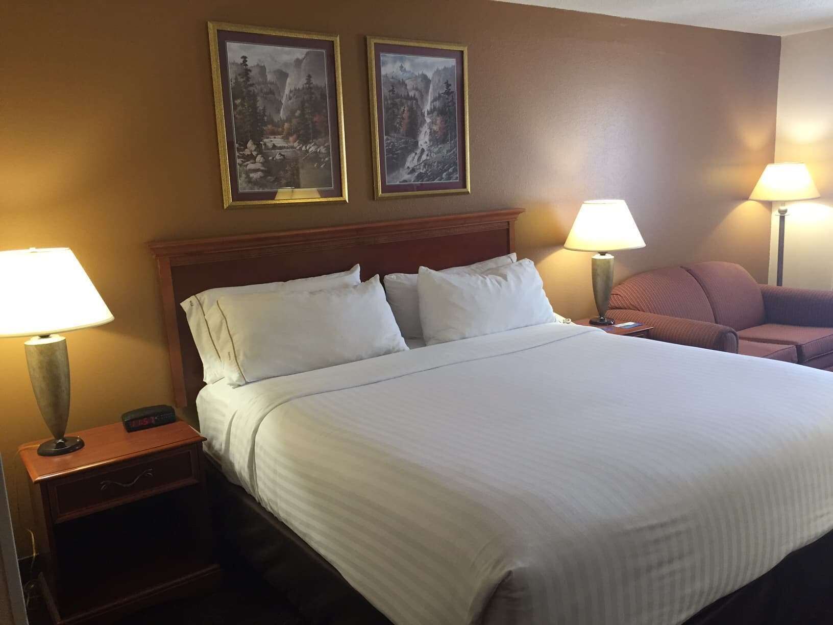 A hotel room with a large bed, two bedside lamps, a nightstand, a chair, and two framed pictures on the wall.
