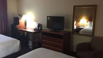 Habitación de hotel con dos camas, un escritorio con computadora y lámpara, un televisor, un espejo y una silla.