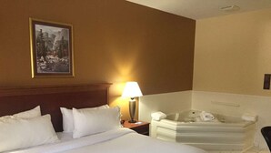 Une chambre d’hôtel avec un grand lit, un coin salon avec un fauteuil, une baignoire et un tableau encadré au mur.