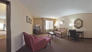 A hotel room with a bed, a desk, two chairs, a television, and a window with curtains.