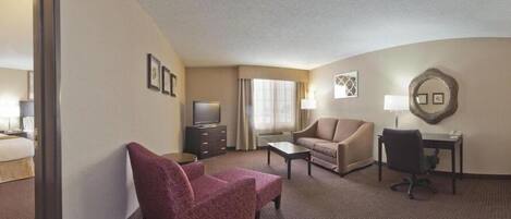 Ein Hotelzimmer mit Bett, Schreibtisch, zwei Stühlen, Fernseher und einem fensterbepflegten Fenster.