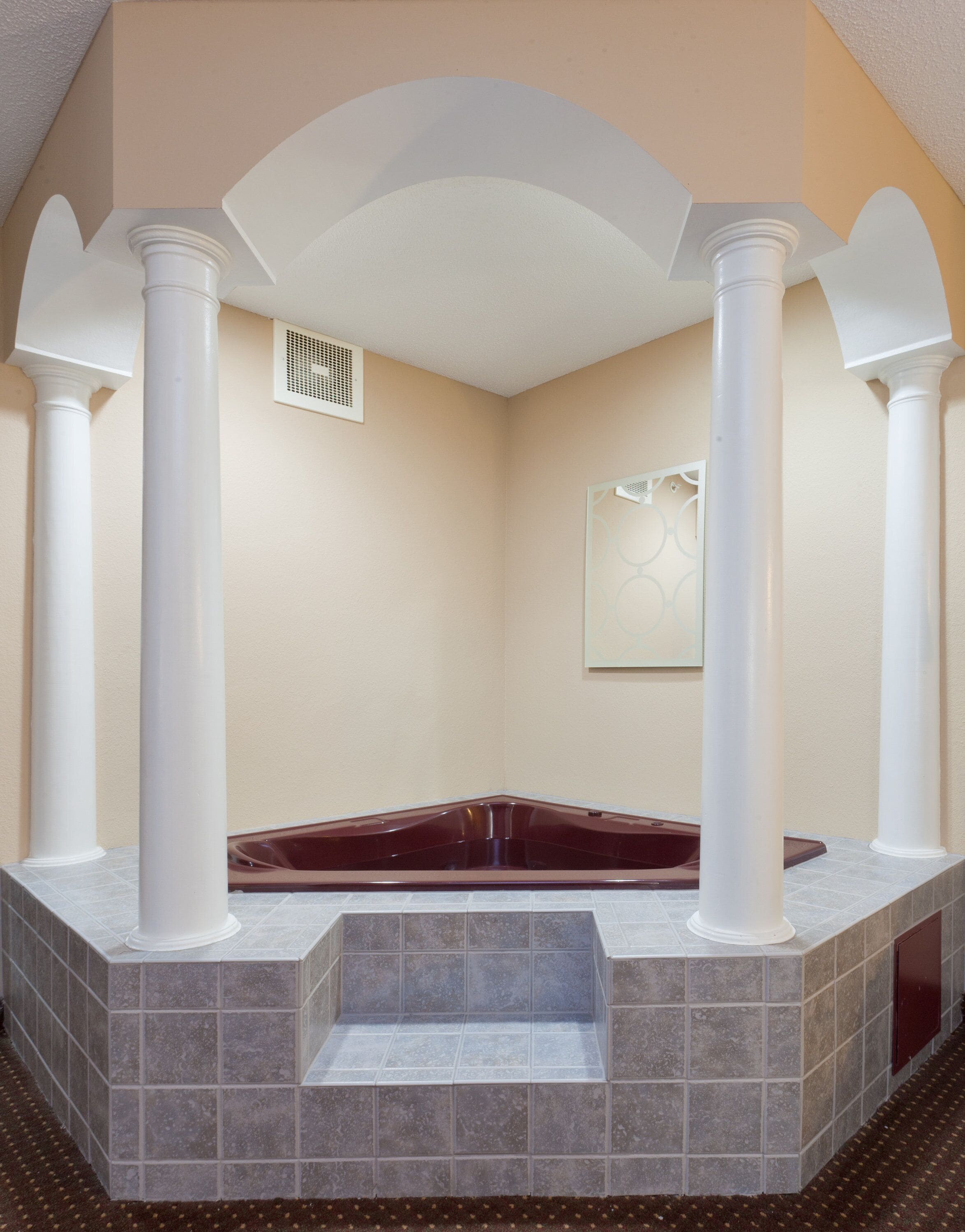 A spa room with a marble bathtub, white columns, and a tiled floor.