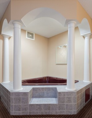 A spa room with a marble bathtub, white columns, and a tiled floor.