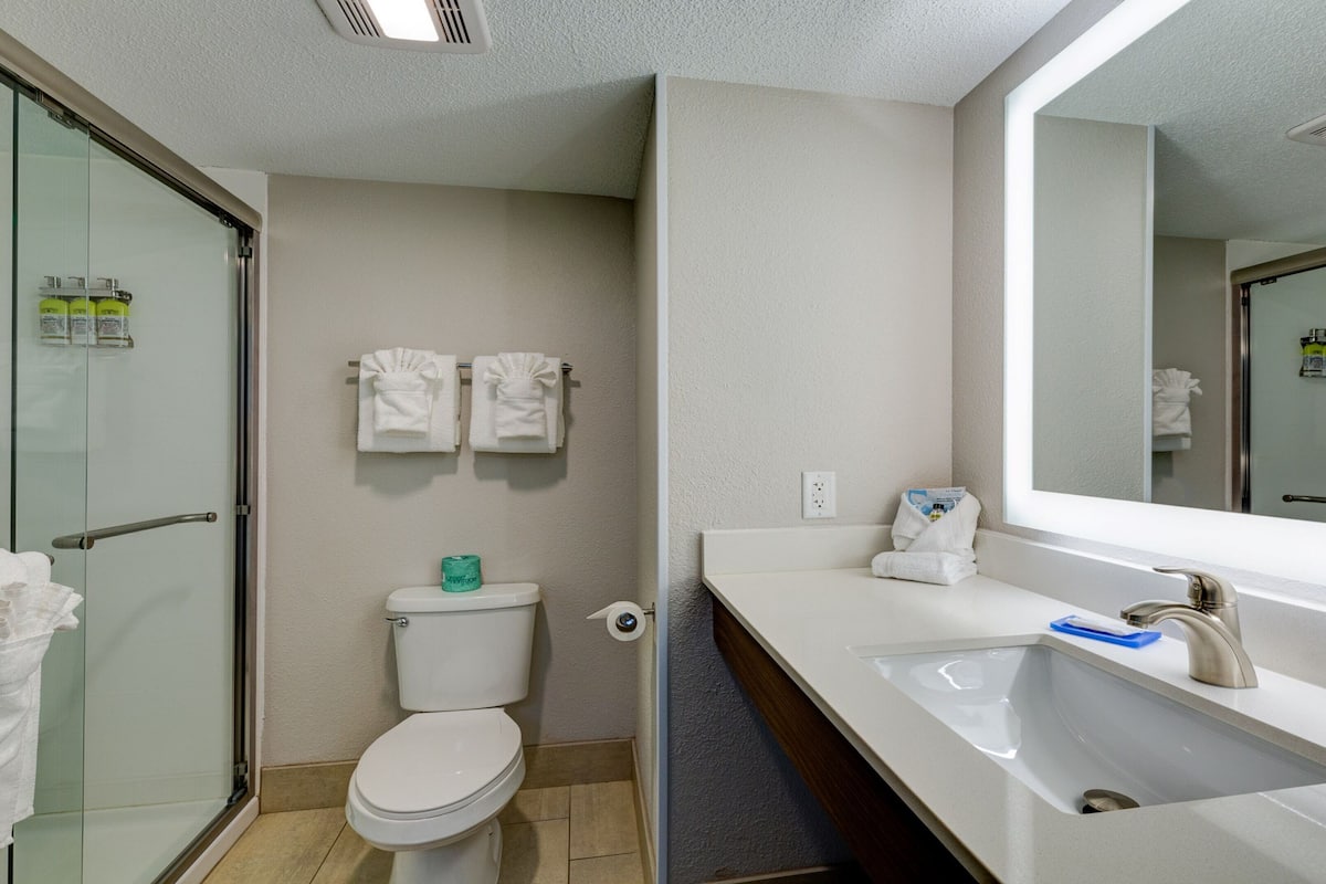 Ein modernes Badezimmer mit Duschkabine aus Glas, Toilette, Waschbecken mit Spiegel und zwei weißen Handtüchern, die an der Wand hängen.