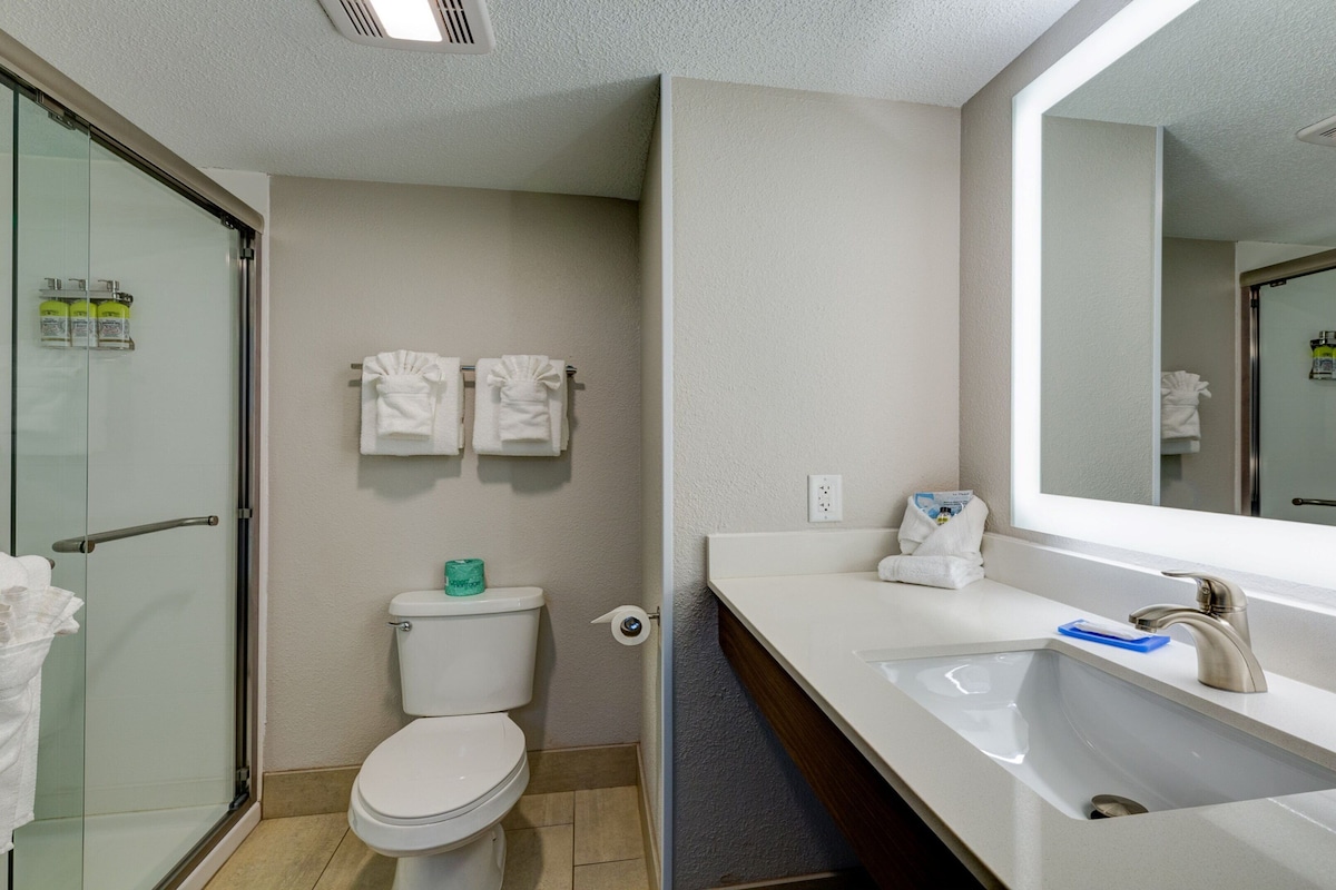 A modern bathroom with a glass shower enclosure, a toilet, a sink with a mirror, and two white towels hanging on the wall.