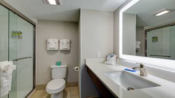 A modern bathroom with a glass shower enclosure, a toilet, a sink with a mirror, and two white towels hanging on the wall.