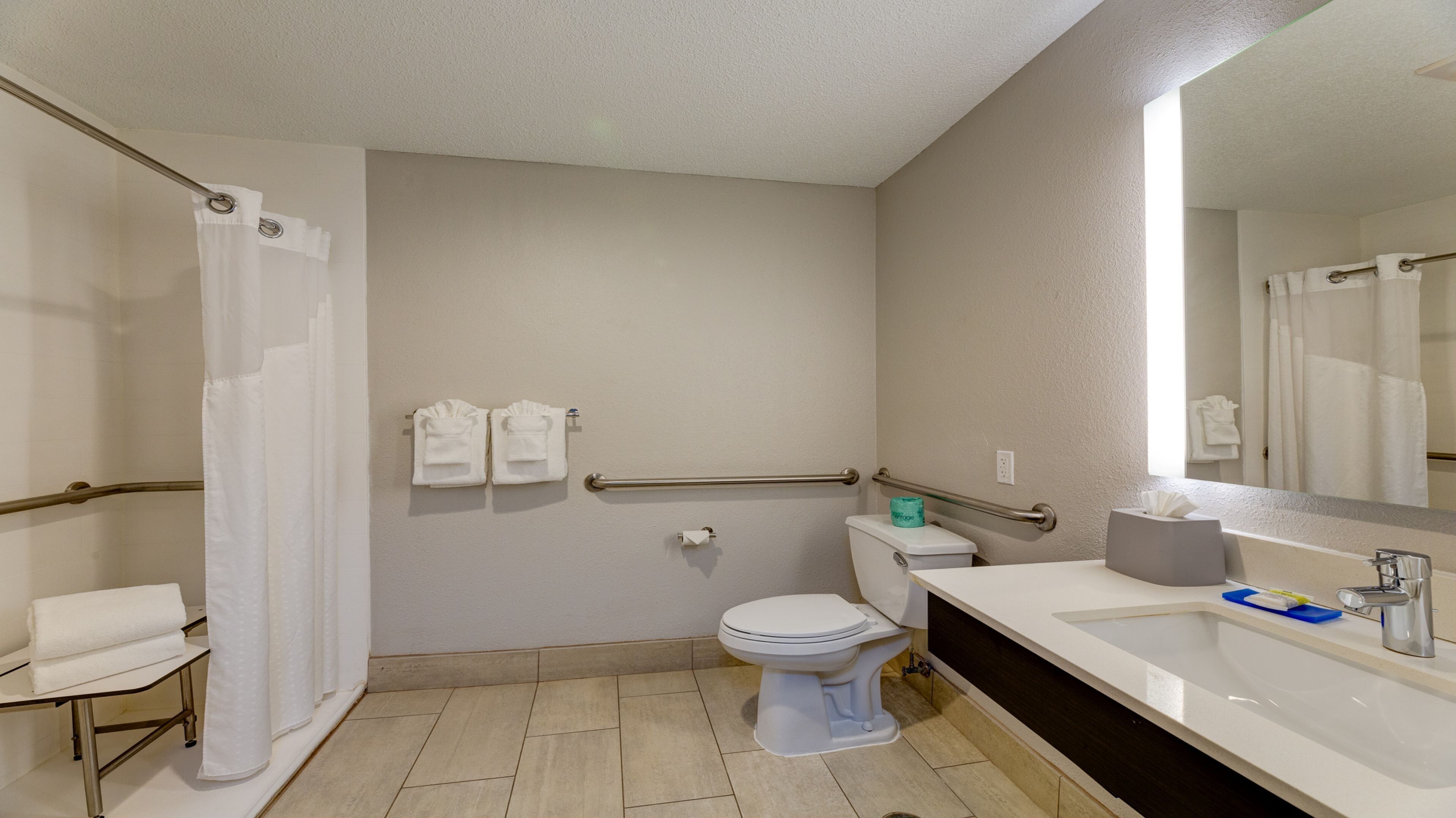 A bathroom with a toilet, sink, and shower. There are towels hanging on a rack and a mirror above the sink.