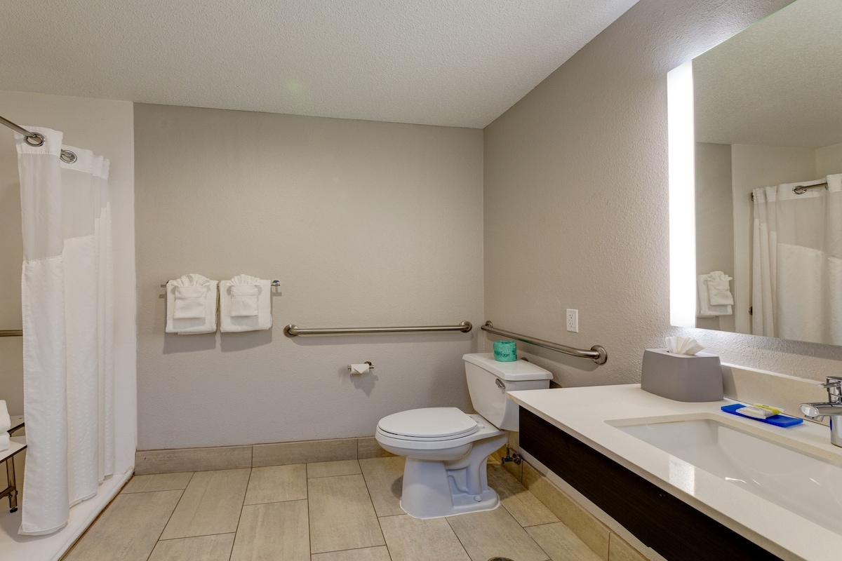 A bathroom with a toilet, sink, and shower. There are towels hanging on a rack and a mirror above the sink.