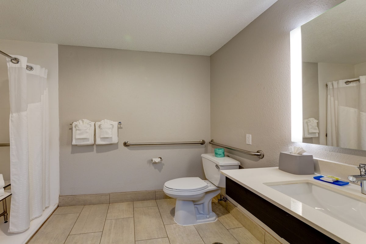 Ein Badezimmer mit Toilette, Waschbecken und Dusche. Handtücher hängen an einem Wäscheständer, und über dem Waschbecken befindet sich ein Spiegel.