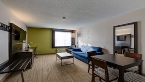 A hotel room with a sofa, a dining table, a TV, and a large window.