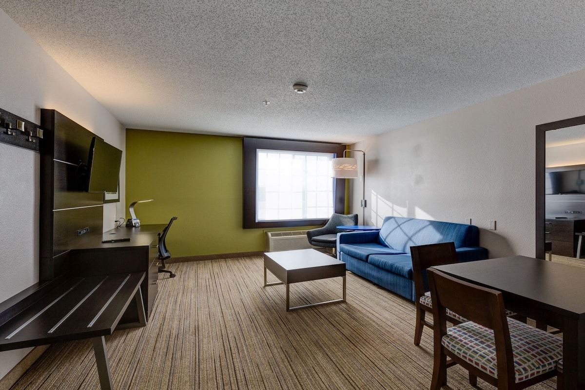 Ein Hotelzimmer mit einer Couch, einem Esstisch, einem Fernseher und einem großen Fenster.