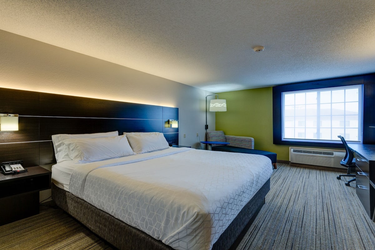 Ein Hotelzimmer mit einem großen Bett, Nachttischen, einem Schreibtisch mit Computer, einem Sessel und einem Fenster mit Blick.