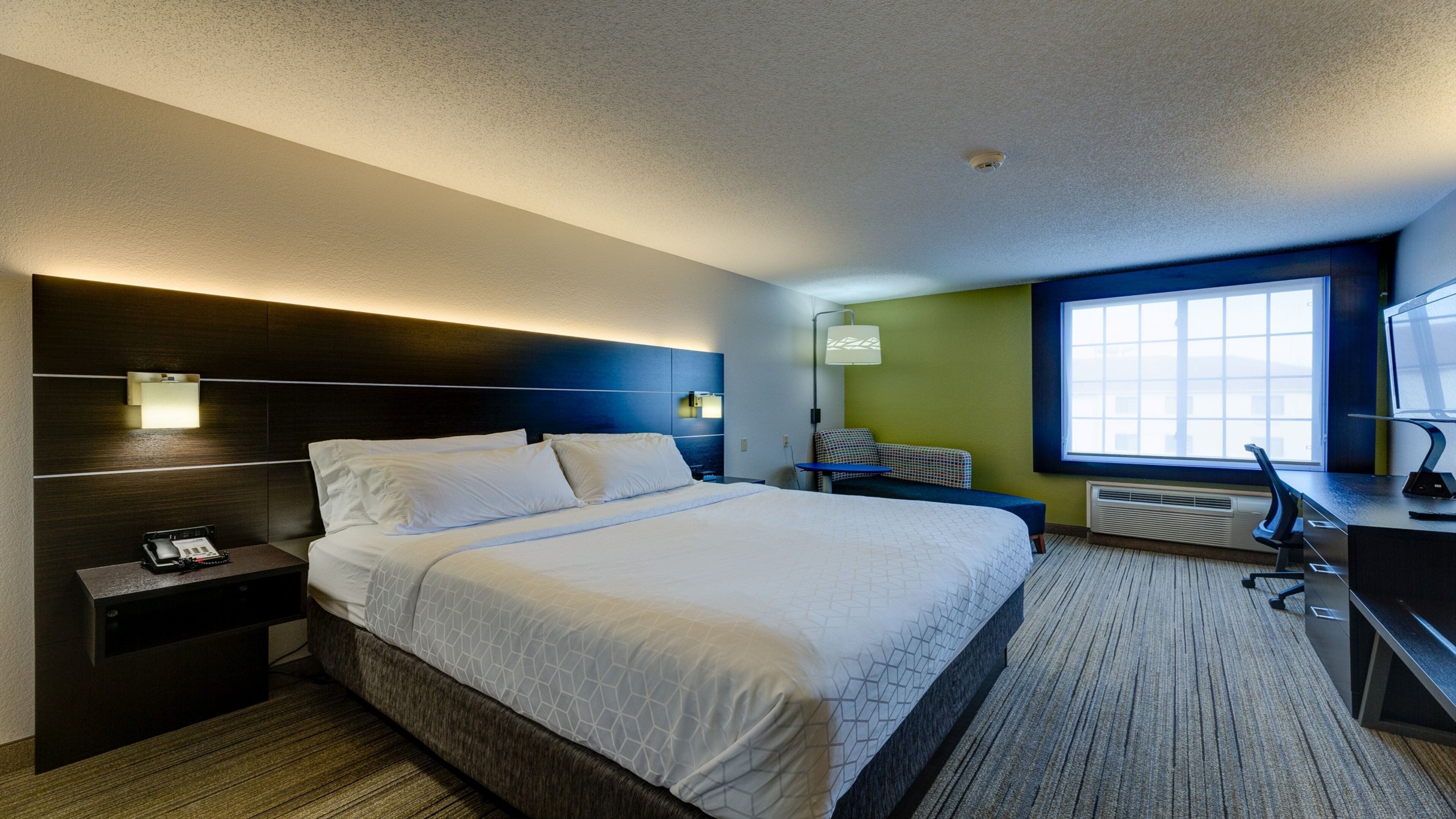 Een hotelkamer met een groot bed, nachtkastjes, een bureau met een computer, een stoel en een raam met uitzicht.