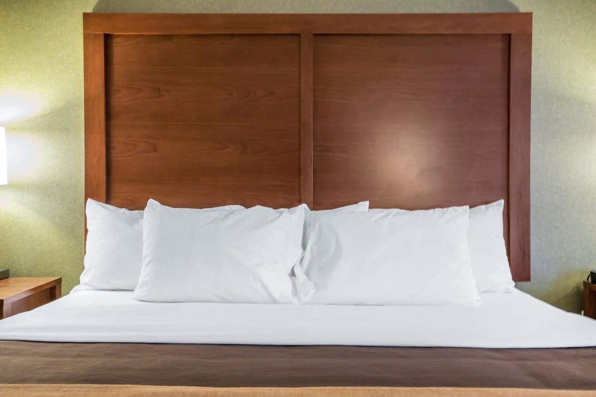 A neatly made bed with white linens and pillows, a wooden headboard, and a brown patterned bedspread.